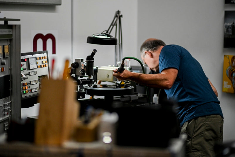 Scott Hull inspecting the stylus-groove interface while cutting, and holding a blow gun and hose for compressed nitrogen on one hand, in front of his Neumann VMS-82 lathe at Masterdisk. Courtesy of Scott Hull.
